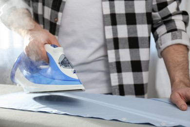 Photo of Man ironing clean shirt at home, closeup