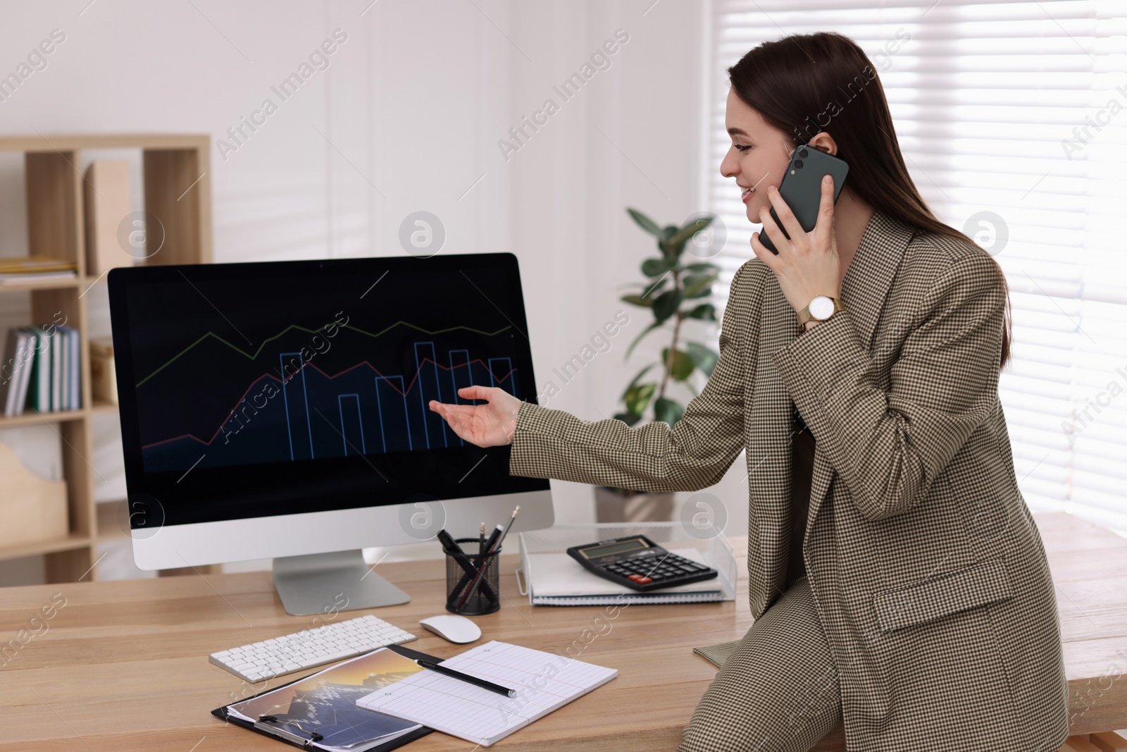 Photo of Businesswoman talking on phone while working with computer in office. Forex trading