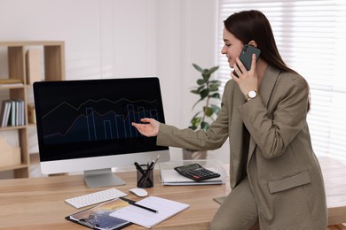 Photo of Businesswoman talking on phone while working with computer in office. Forex trading