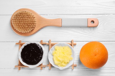 Photo of Natural body scrubs, orange and brush on white wooden table, flat lay. Anti cellulite treatment
