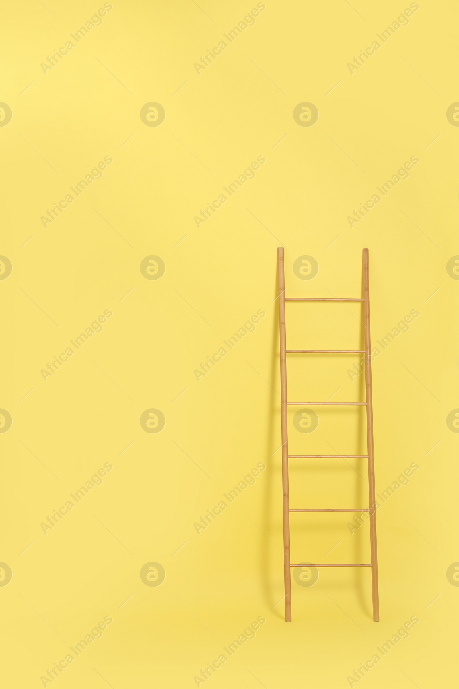 Photo of Modern wooden ladder on yellow background. Space for text