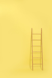 Photo of Modern wooden ladder on yellow background. Space for text