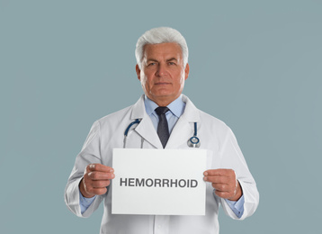 Doctor holding sign with word HEMORRHOID on light grey background