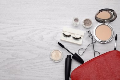 Photo of Cosmetic bag with eyelash curler and makeup products on white wooden table, flat lay. Space for text