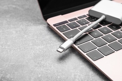 Photo of USB cable with type C connector and laptop on grey table, closeup. Space for text