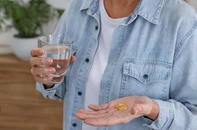 Woman with vitamin pills and glass of water indoors, closeup