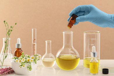 Photo of Scientist developing cosmetic oil at white table, closeup