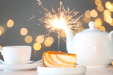 Photo of Cake with burning sparkler on table against blurred festive lights