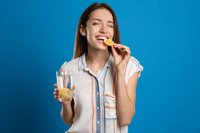 Photo of Young woman with glass of lemon water on light blue background