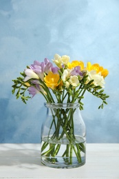 Bouquet of fresh freesia flowers in vase on table. Space for text