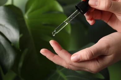 Photo of Woman applying cosmetic serum onto finger on blurred background, closeup. Space for text
