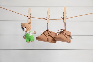 Photo of Cute baby shoes and crochet toy drying on washing line against white wall