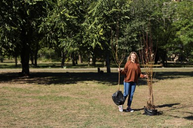 Happy woman with young trees ready for planting outdoors on sunny day