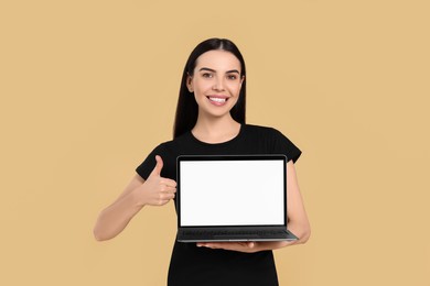 Happy woman with laptop showing thumb up on beige background