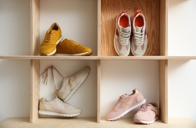 Wooden shelving unit with stylish women's sneakers on white wall