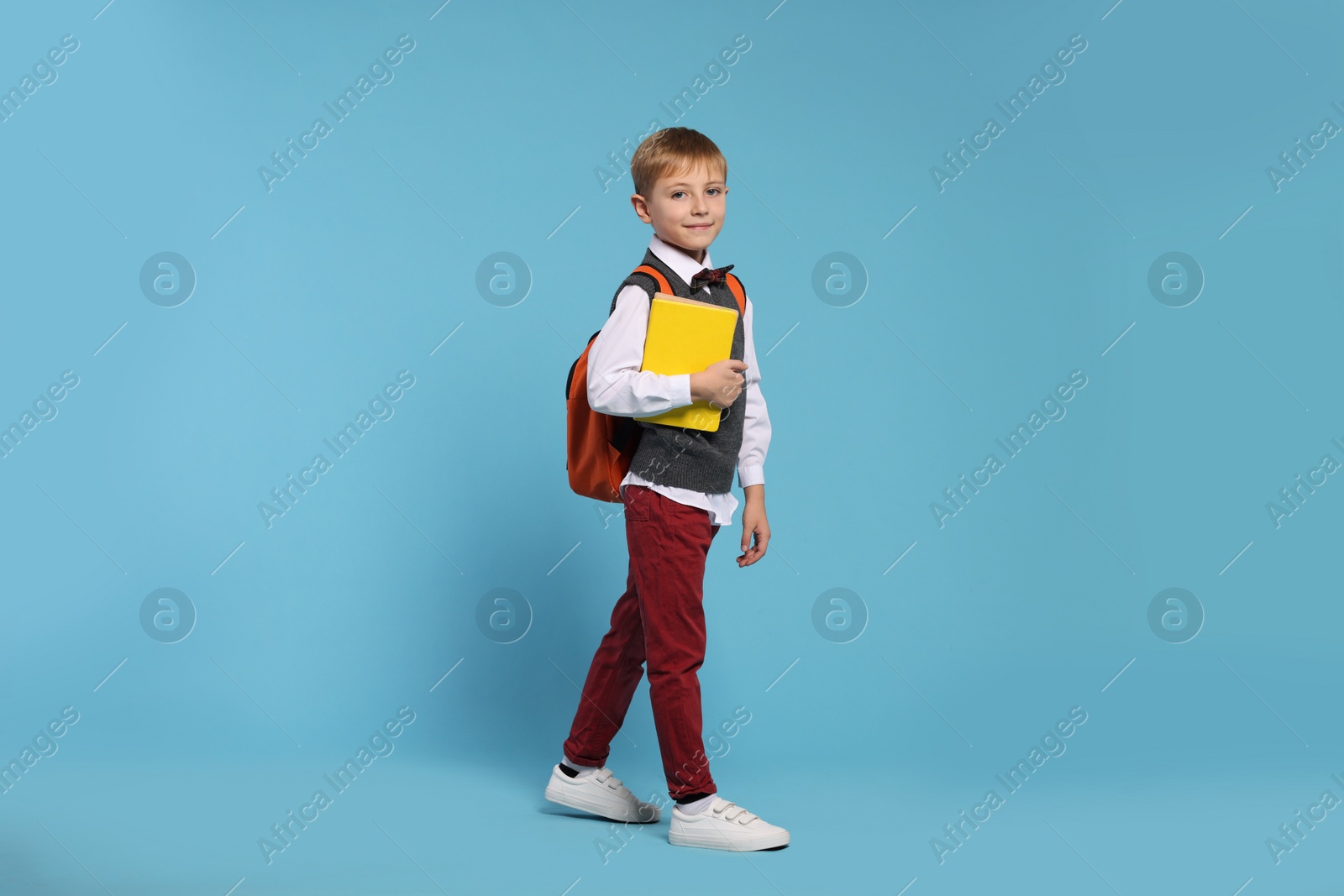 Photo of Happy schoolboy with backpack and books on light blue background