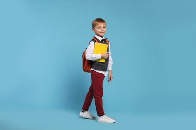 Happy schoolboy with backpack and books on light blue background