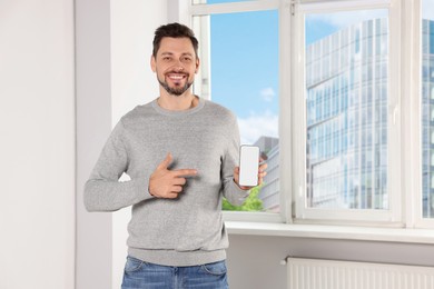 Happy man with phone near window indoors, space for text