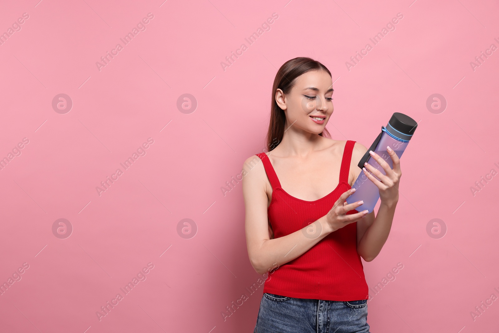 Photo of Beautiful young woman with transparent bottle on pink background, space for text