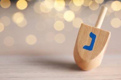 Hanukkah traditional dreidel with letter Nun on wooden table against blurred lights, closeup. Space for text