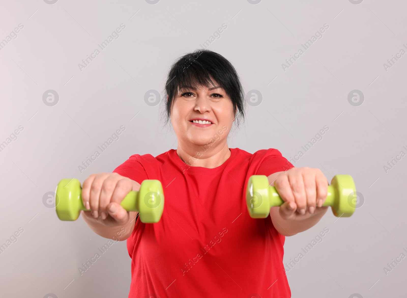 Photo of Happy overweight mature woman doing exercise with dumbbells on grey background