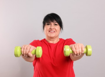 Photo of Happy overweight mature woman doing exercise with dumbbells on grey background