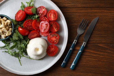 Photo of Delicious burrata cheese with tomatoes and arugula served on wooden table, top view