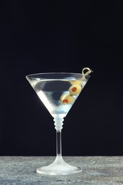 Photo of Martini cocktail with olives on grey table against dark background, space for text