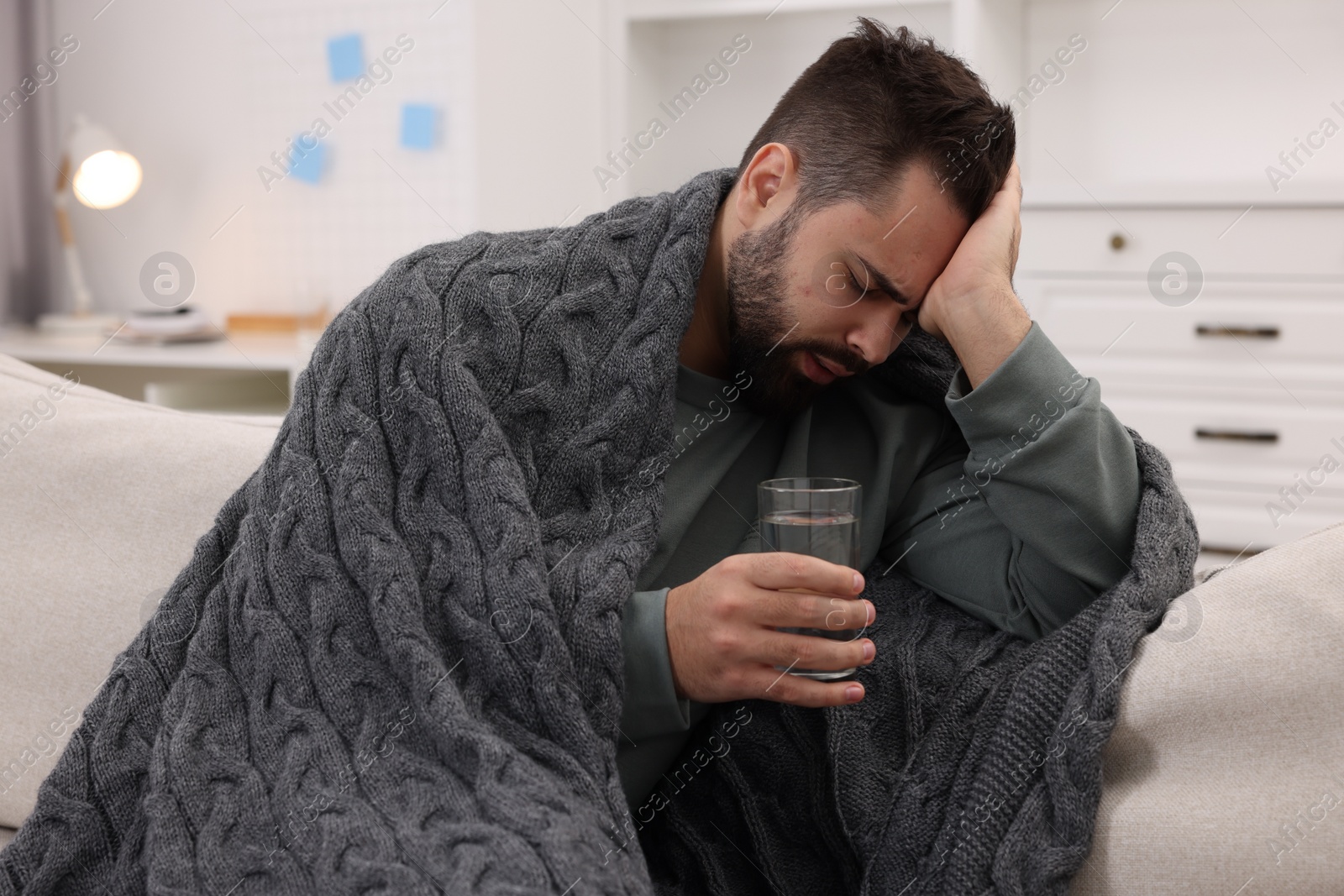 Photo of Man with glass of water suffering from headache on sofa at home