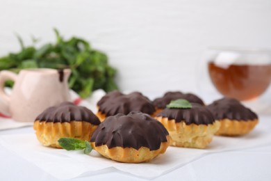 Photo of Delicious profiteroles with chocolate spread and mint on white table