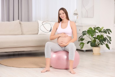 Pregnant woman sitting on fitness ball at home. Doing yoga