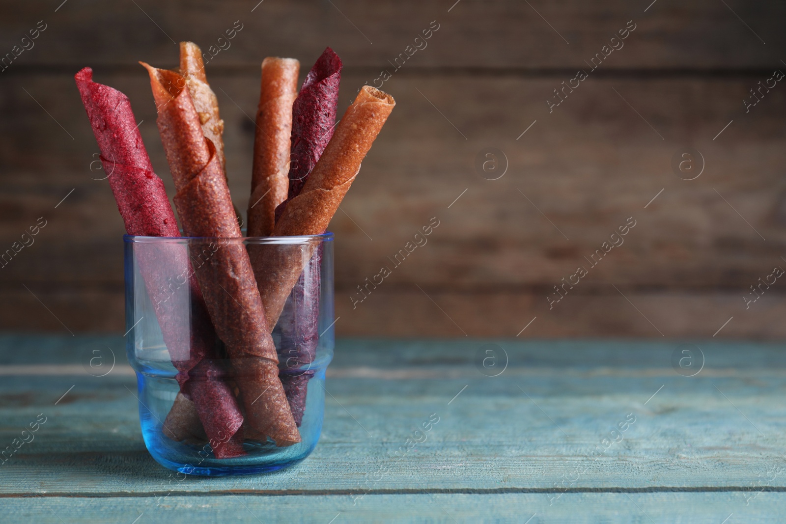 Photo of Delicious fruit leather rolls on blue wooden table. Space for text