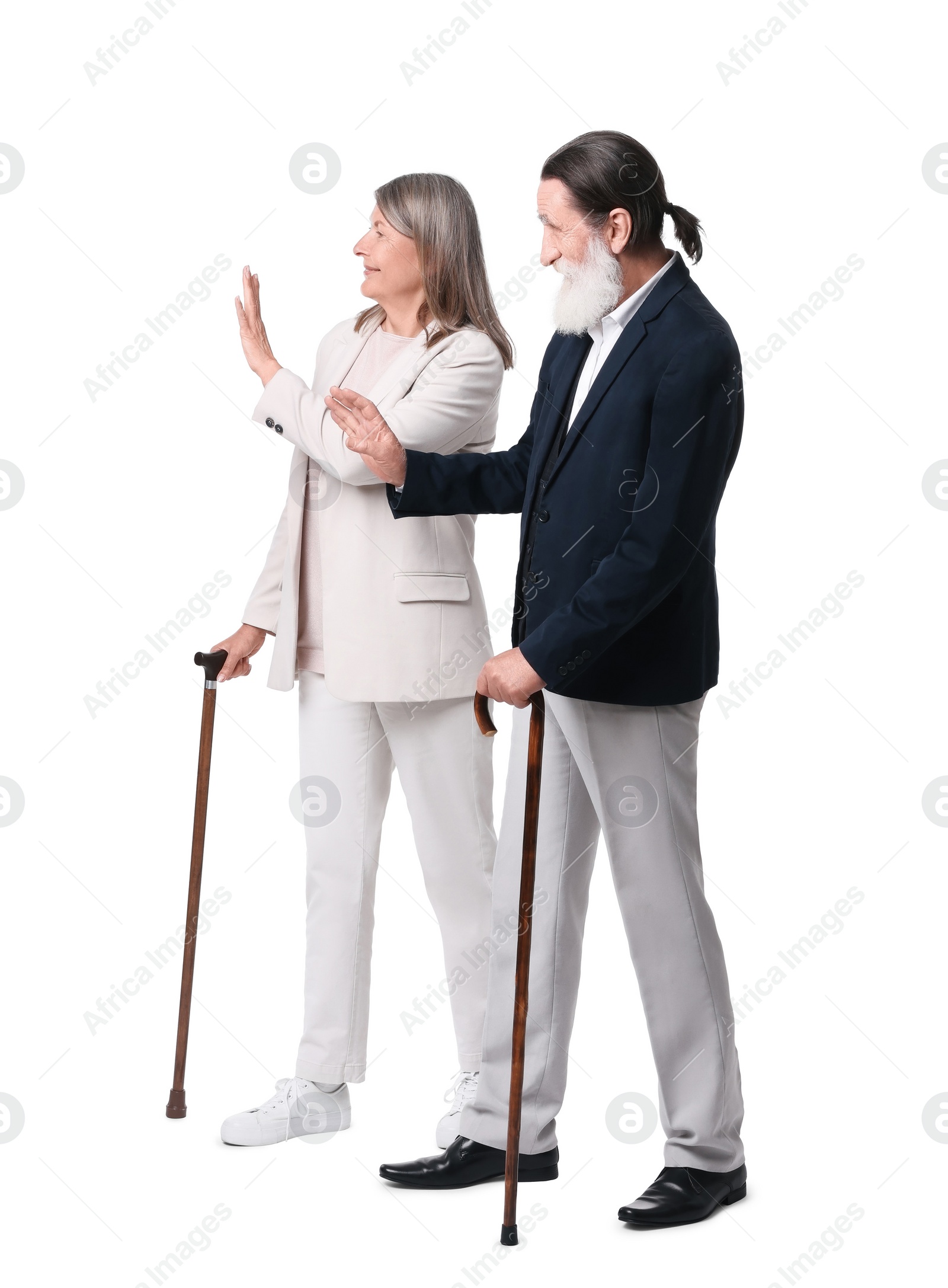 Photo of Senior man and woman with walking canes greeting someone on white background
