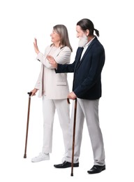 Senior man and woman with walking canes greeting someone on white background