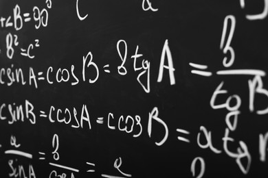 Different mathematical formulas written with chalk on blackboard, closeup