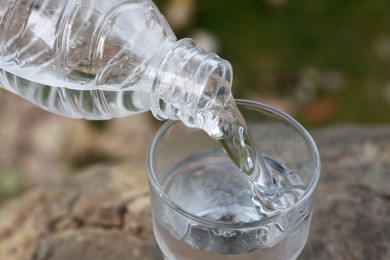 Photo of Pouring water from bottle into glass outdoors, closeup
