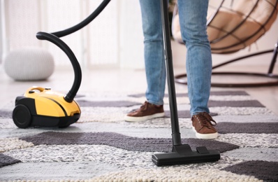 Young man cleaning carpet with vacuum cleaner at home, closeup