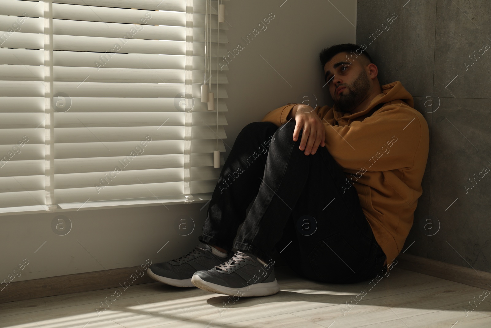 Photo of Sad man sitting on floor near window. Space for text