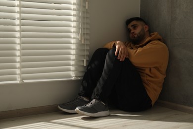 Photo of Sad man sitting on floor near window. Space for text