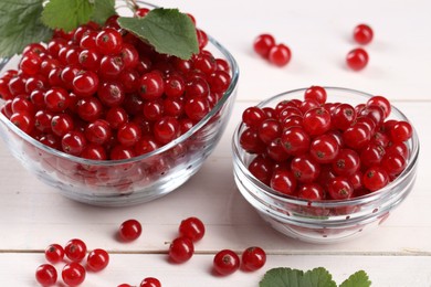 Photo of Many ripe red currants and leaves on white wooden table