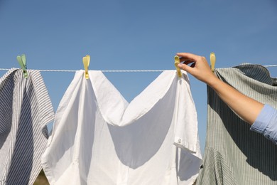 Photo of Woman hanging clothes with clothespins on washing line for drying under blue sky outdoors, closeup