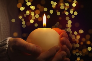 Image of Closeup view of woman holding burning candle in darkness, bokeh effect. Christmas Eve