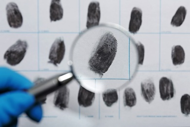 Criminalist exploring fingerprints with magnifying glass, closeup