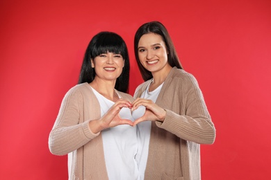Photo of Young daughter and her mature mother making heart with their hands on color background