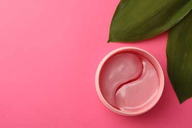 Photo of Jar of under eye patches and green leaves on pink background, flat lay with space for text. Cosmetic product