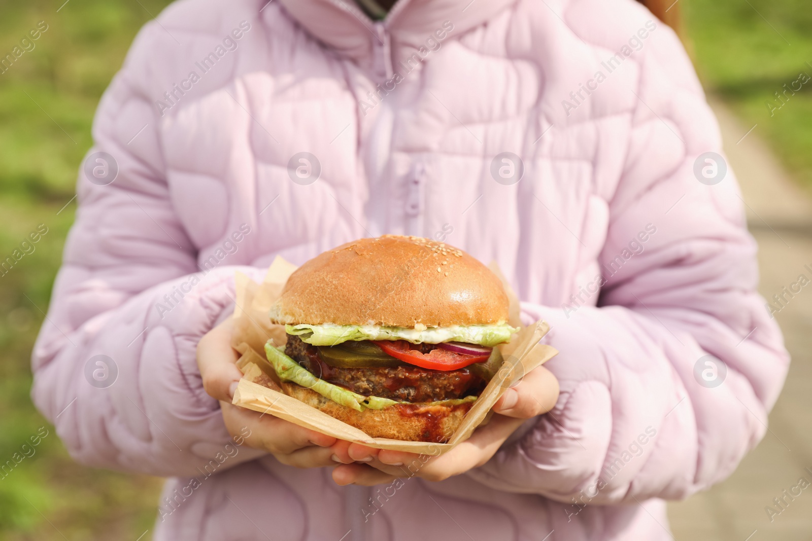 Photo of Little girl holding fresh delicious burger outdoors, closeup. Street food