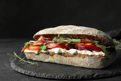 Photo of Delicious sandwich with fresh vegetables and prosciutto on black table