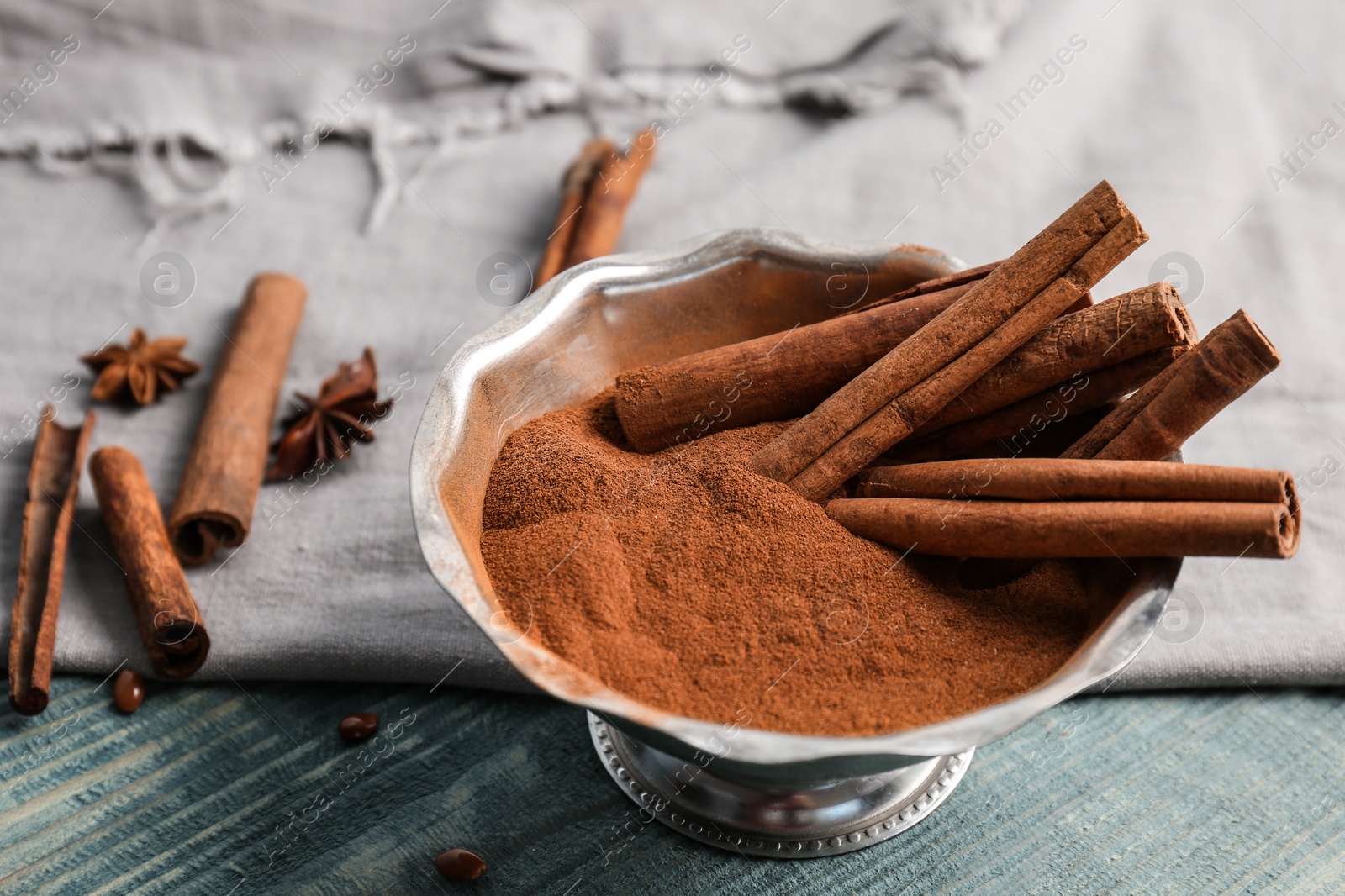 Photo of Bowl with aromatic cinnamon powder and sticks on wooden background