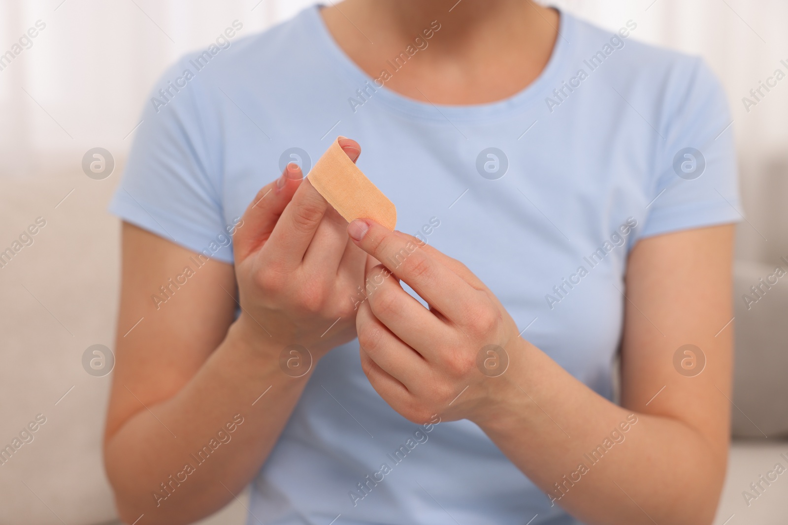Photo of Woman putting sticking plaster onto finger indoors, closeup