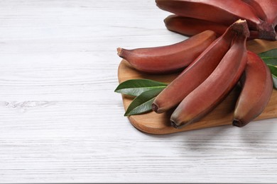 Tasty red baby bananas on white wooden table, space for text